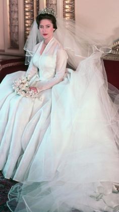 a woman in a wedding dress and veil sitting on a couch wearing a tiara