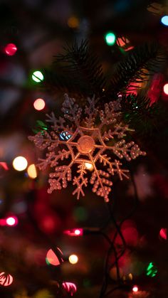 a snowflake ornament on a christmas tree with lights in the background