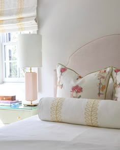 a bed with white sheets and pink headboard in front of a window next to a lamp