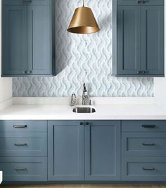 a kitchen with blue cabinets and a gold pendant light hanging over the sink in front of it