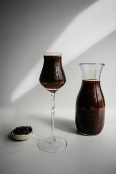 two glasses filled with liquid sitting next to each other on a white surface, one has a spoon in it and the other is empty