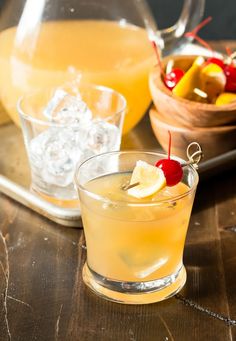 two glasses filled with lemonade and cherries on top of a wooden table next to an ice bucket