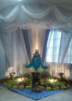 a table topped with lots of fruit under a canopy covered by curtains and lights in front of a window