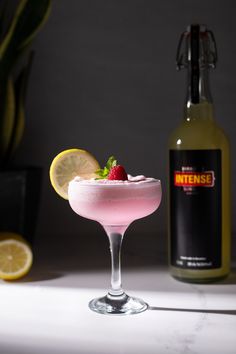 a pink cocktail garnished with raspberries and limes next to a bottle of lemonade