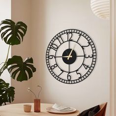 a clock is on the wall next to a potted plant and a table in front of it