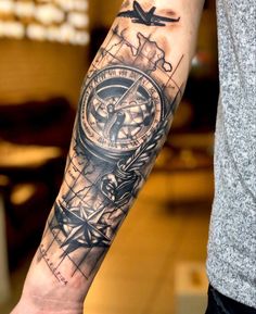 a man's arm with a compass and plane tattoo on the left side of his arm