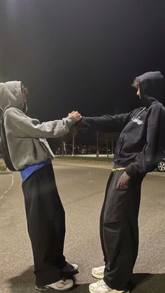 two young men standing in the middle of an empty parking lot, one wearing a hoodie and the other holding hands