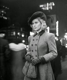 a woman in a coat and hat standing on the street