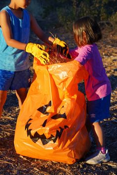 two young children are playing with an orange bag full of pumpkins on the ground