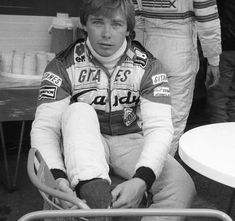 a man sitting on top of a chair next to another person in a race uniform