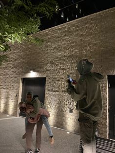 two people standing in front of a building at night, one holding a child and the other using a cell phone