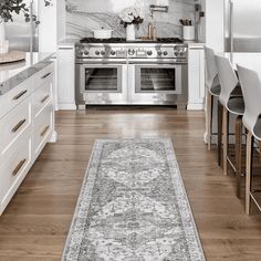 a kitchen with white cabinets and an area rug on the floor in front of the stove