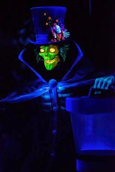 a man in a top hat and green face painted with neon blue lights is standing next to a bucket