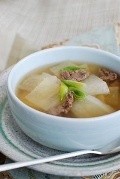 a white bowl filled with soup and meat on top of a tablecloth next to a napkin