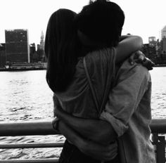 black and white photograph of two people embracing each other on a bridge near the water