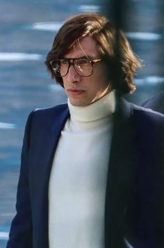 a man with glasses walking next to another man in a suit and turtle neck sweater