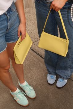 two people standing next to each other holding yellow purses and shoes on their feet