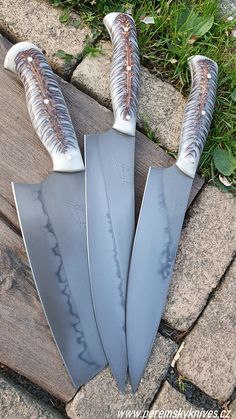 four knives are laying on the ground in front of some grass and rocks, with one knife sticking out of it's blades