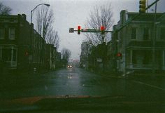 an empty street with stop lights and buildings in the background on a gloomy day