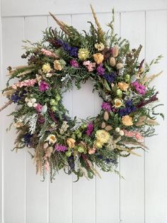 a wreath hanging on the side of a door with flowers and greenery around it