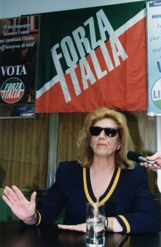 a woman sitting at a table in front of a microphone with her hands out to the side