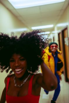 two people walking down a hallway with one holding her hair in the air and smiling