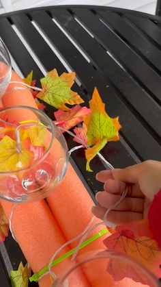 someone is holding some orange candles on a table with autumn leaves around them and wine glasses in the foreground