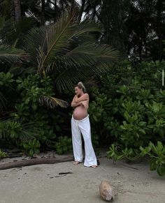 a pregnant woman standing on the beach with her arms crossed