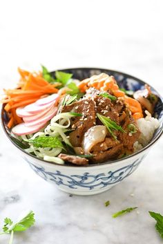 a blue and white bowl filled with meat, veggies and onions on top of a marble counter