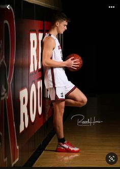 a young man holding a basketball standing next to a wall