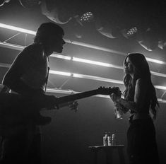 black and white photo of two people playing guitars in a dark room with spotlights