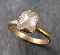 a gold ring with a white diamond in the center on a gray surface, close up