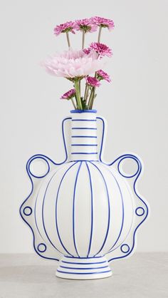 a blue and white vase with some pink flowers in it's bottom half, sitting on a table