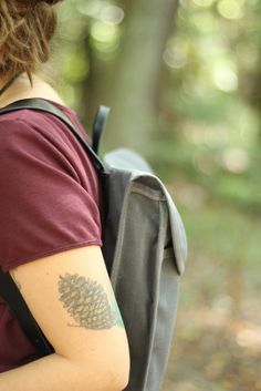 a woman with a tattoo on her arm is holding a backpack in the woods,