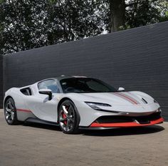 a white and red sports car parked in front of a black wall with trees behind it