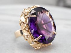 "This amethyst statement ring is a real showstopper! The mounting is ornate and botanically inspired, with leaves and berry accents that could almost be plucked from a garden. The centerpiece is a royal purple amethyst, glittering from every angle and rich with pinkish violet undertones. Metal: 18K Yellow Gold Gem: Amethyst 30.30 Carats Gem Measurements: 19.8 x 24.6 mm, Oval Ring Size: 7.50 Marks: \"18K\" Stamped on the inside band SKU #: 675VFPRE Each piece has been identified and graded by a G Yellow Gold Amethyst Ring, Amethyst Cocktail Ring, Gold Amethyst Ring, Right Hand Ring, Gold Statement Ring, Amethyst Gem, Amethyst Gold, Right Hand Rings, Hand Ring