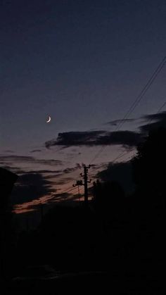 the moon is seen in the night sky with power lines and telephone poles behind it