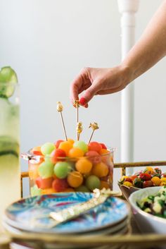 a person reaching for some fruit on a stick in front of a bowl of salad