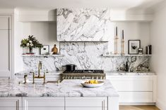 a white kitchen with marble counter tops and gold faucets on the stove top