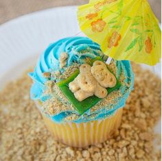 a cupcake with blue frosting and a yellow umbrella on top is sitting on a plate