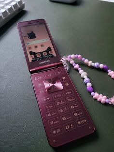 a purple cell phone sitting on top of a table next to a beaded necklace