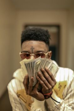 a man holding money in his hands while wearing glasses and a white shirt with writing on it