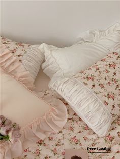 a bed with white pillows and pink flowers on the comforter next to a teddy bear