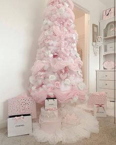 a pink christmas tree decorated with white and pink flowers, bows and other accessories in a room