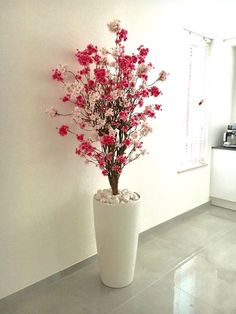 a white vase with pink flowers in it on the floor next to a kitchen counter