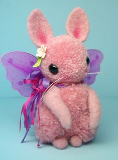 a pink stuffed animal with purple wings and a flower in it's hair on a blue background