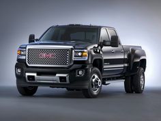 the black truck is parked in front of a gray background and there are two people standing next to it