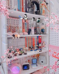 a book shelf filled with lots of books next to a pink flowery tree in front of a white wall