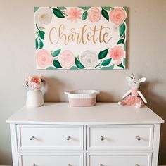 a white dresser with flowers and a sign above it that says charlotte on the wall