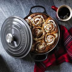 a pan filled with cinnamon rolls next to a cup of coffee on top of a table